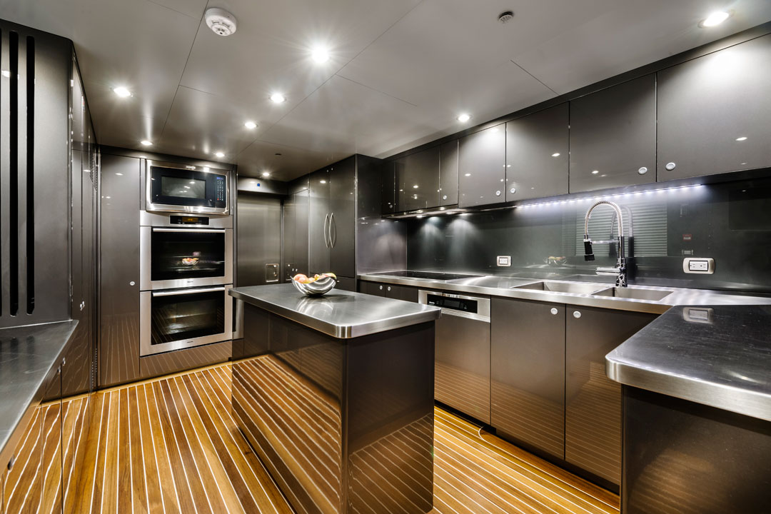Stainless steel superyacht galley with ovens, cooktop, dishwasher and LED under-cabinet lighting on teak decking