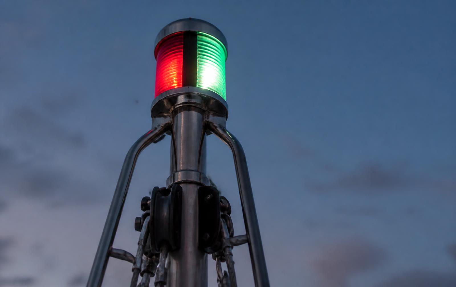 Combination red and green navigation light glowing on a yacht mast at dusk